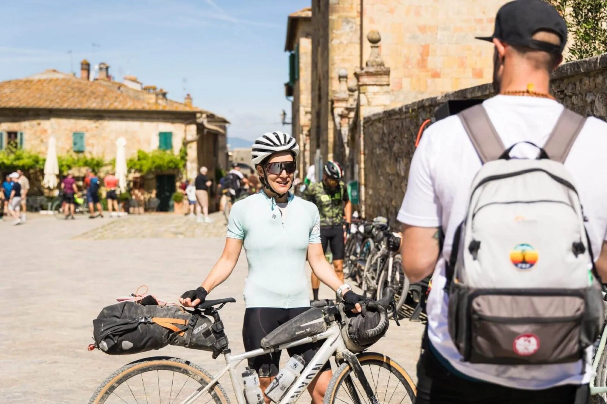 Una partecipante con la bici gravel carica di borse da bikepacking in una piazza toscana